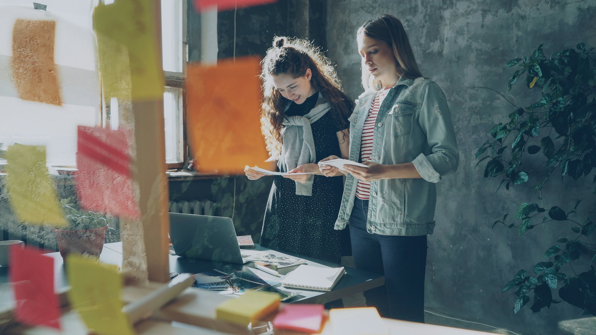 Two colleagues reviewing notes beside a wall of sticky notes